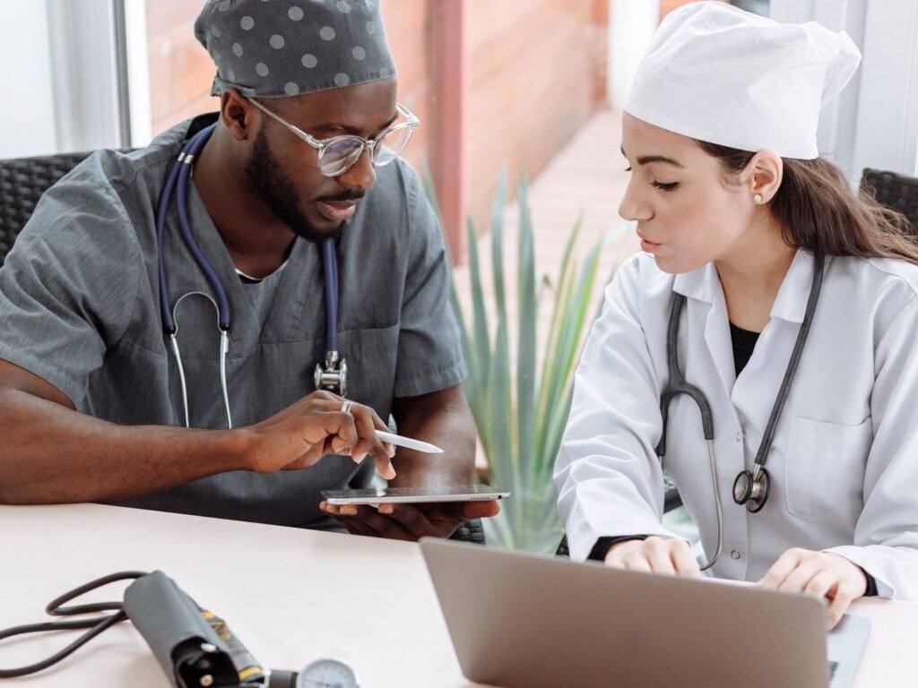 Two medical professionals reviewing information together on a tablet and laptop.